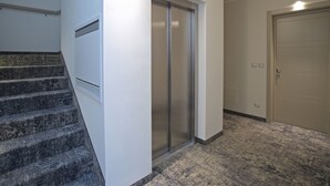 A hallway with a carpeted floor, a staircase with a handrail, a door with a handle, and a wall-mounted vent.