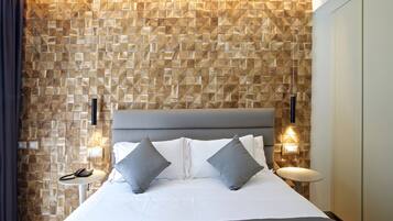A modern hotel room with a geometric patterned wall, a grey upholstered bed with two pillows, bedside lamps, and a small table with a telephone.