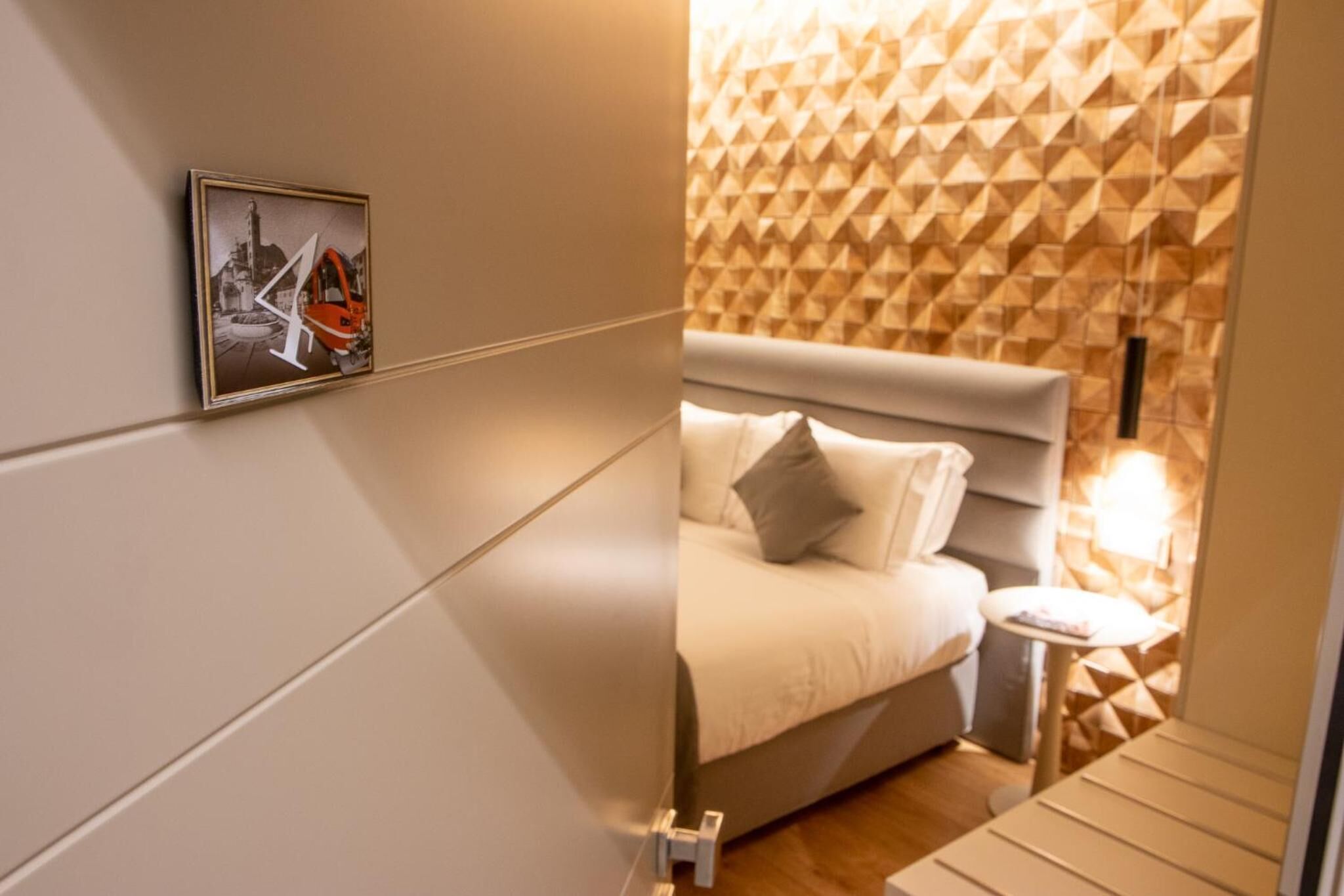 A modern hotel room with a bed, a small bedside table, and a geometric patterned wall.