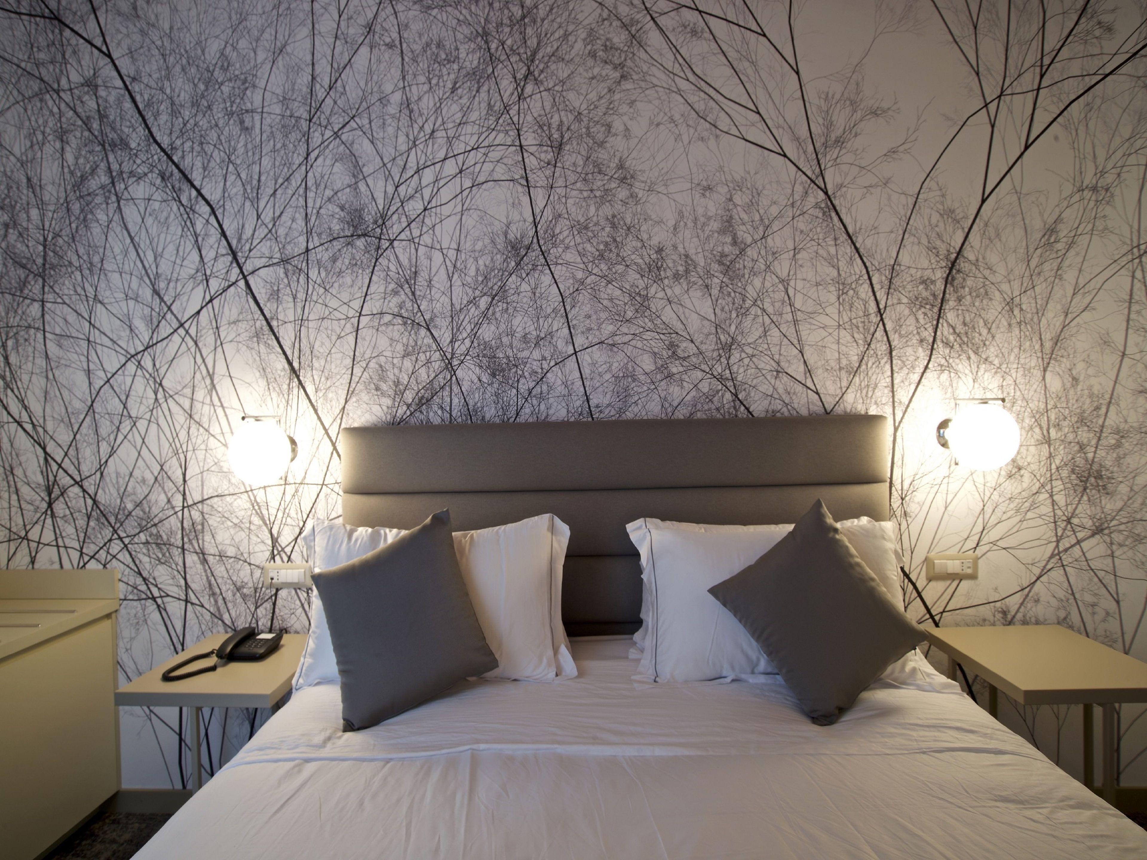 A hotel room with a bed, bedside tables, and a wall with a tree branch pattern.