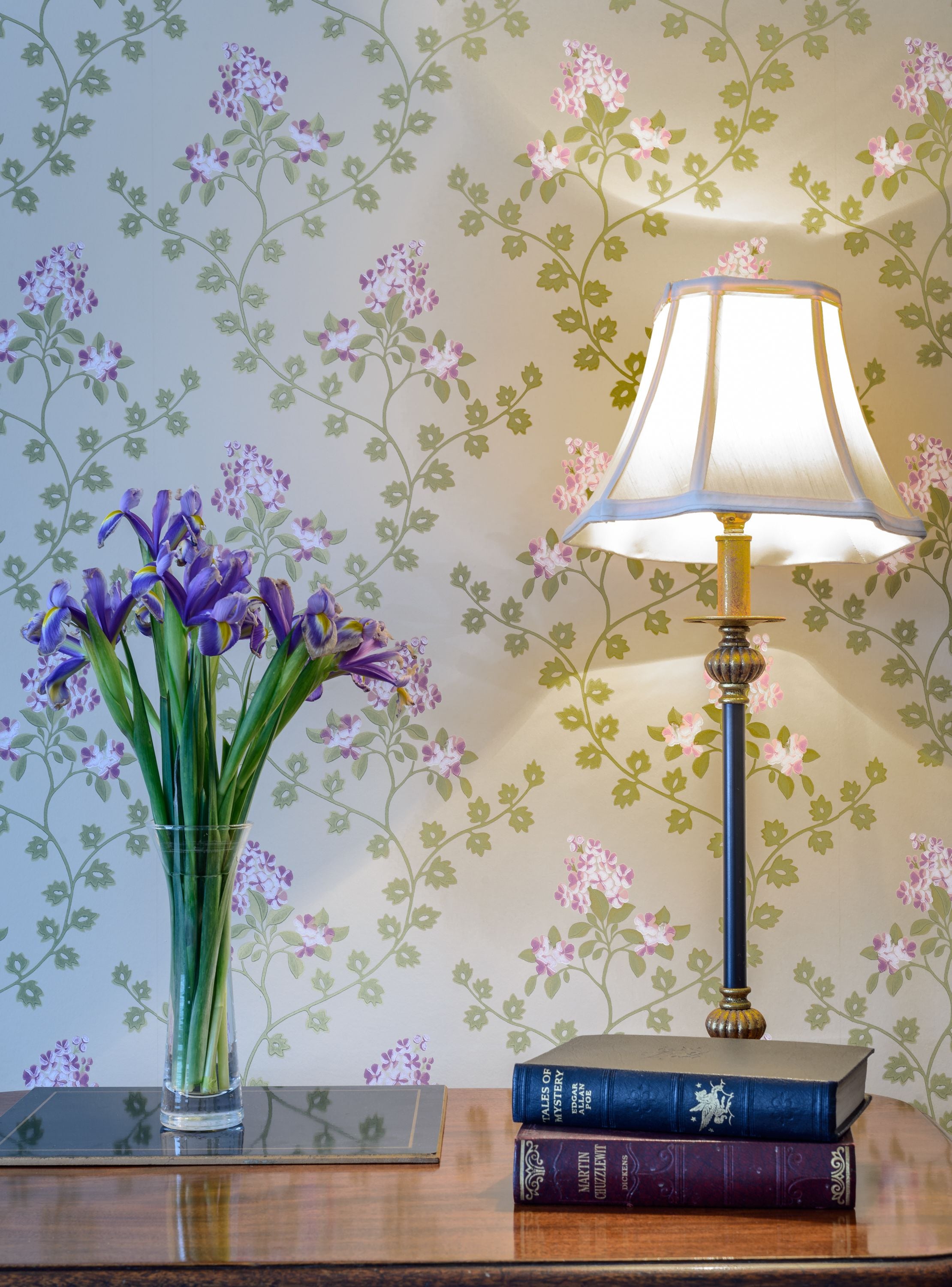 A table with a lamp, a vase with flowers, and books.