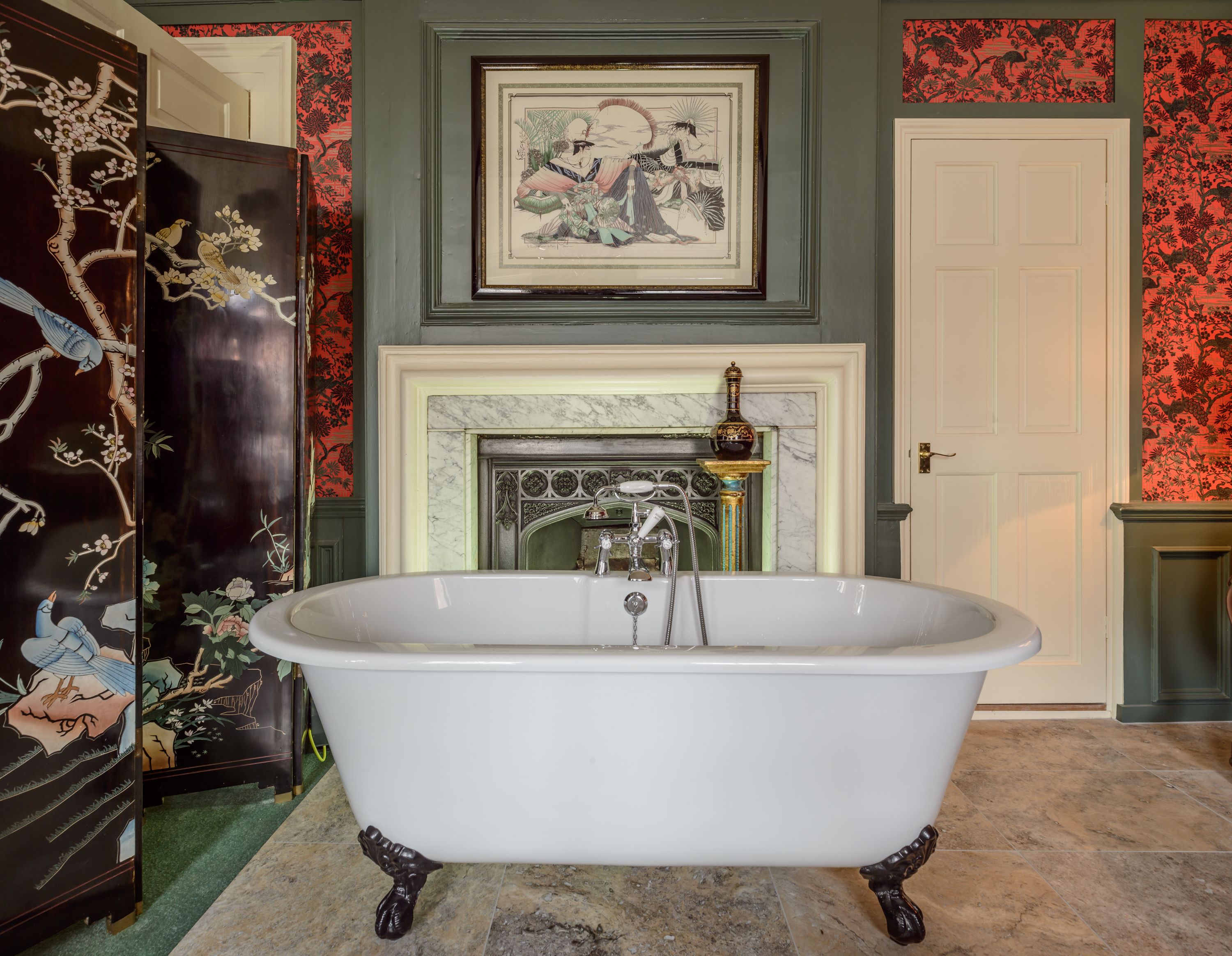A bathroom with a freestanding clawfoot bathtub, a marble fireplace, and traditional wall decor.