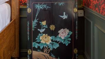 A bedroom with a wooden four-poster bed, a nightstand with a lamp, a decorative vase, and a cabinet with floral artwork.