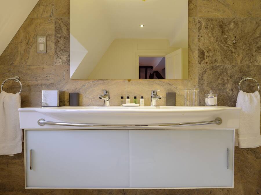 A bathroom with a stone wall, a large mirror, a double sink with a towel ring, and a cabinet below.