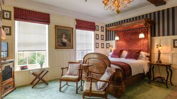 A traditional bedroom with a four-poster bed, two armchairs, a wooden dresser, and a chandelier.