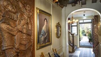 A hallway with a wooden carving, a framed portrait, and a rack of umbrellas.