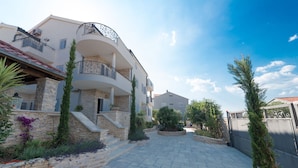 A multi-story residential building with a stone facade, a curved balcony, and a paved courtyard. - Villa Kos (Murter-Kornati)