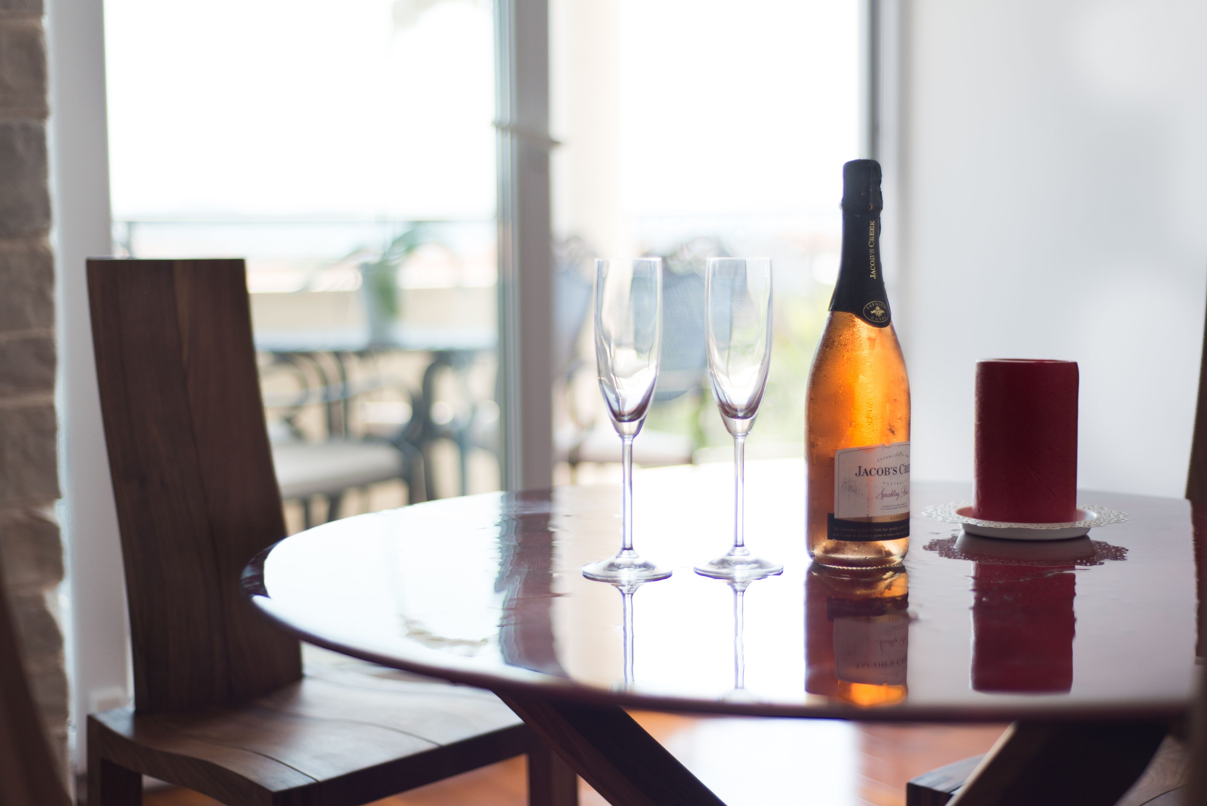 A round table with a bottle of wine, two wine glasses, and a red candle.