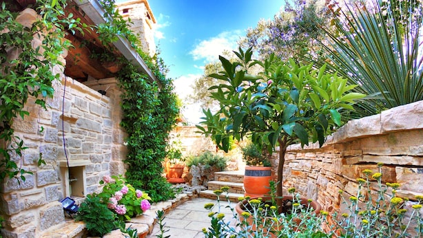 A stone-walled courtyard with a variety of plants and flowers, a small tree, and a stone bench. - Villa Kos (Murter-Kornati)