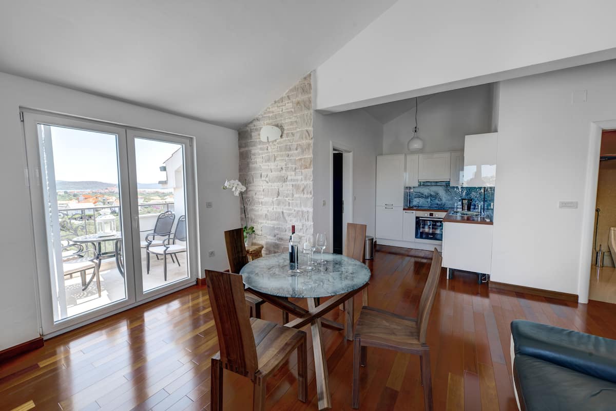 A spacious living area with a round glass table, wooden chairs, and a view through large sliding doors to an outdoor patio.