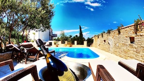 A poolside area with wicker furniture, a bottle of champagne in a bucket, and a stone wall in the background. - Villa Kos (Murter-Kornati)
