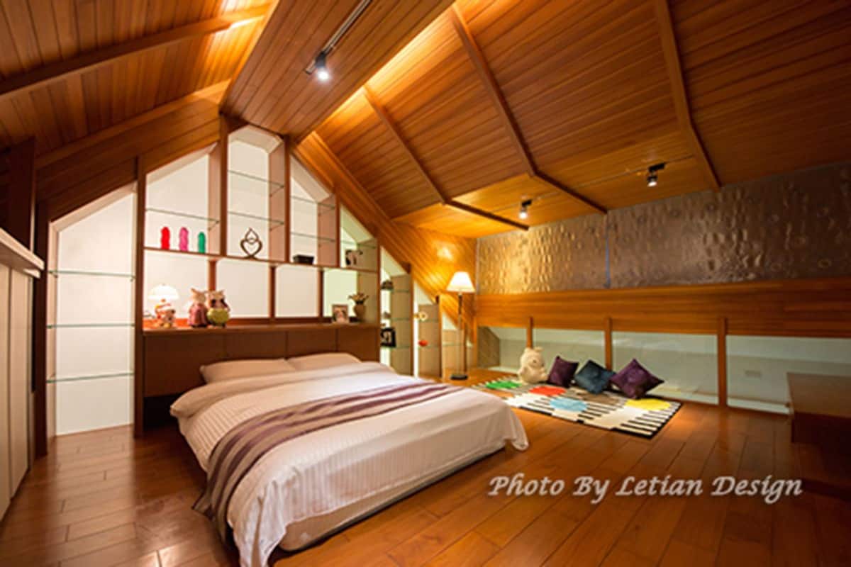 A bedroom with a wooden ceiling, a bed with a striped blanket, a nightstand with a lamp, and a view of the outside through a window.