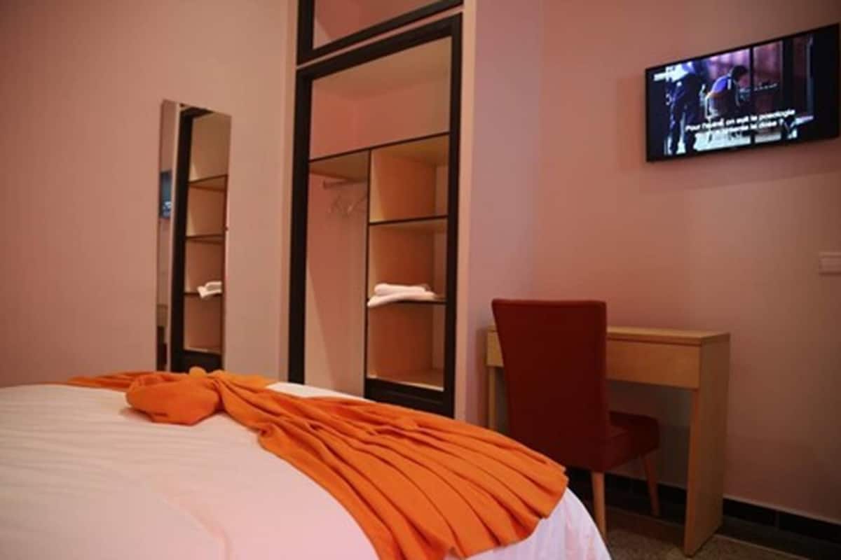 A hotel room with a bed, a desk, a chair, and a TV mounted on the wall.