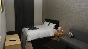 Una habitación de hotel con cama, mesita de noche, lámpara, sofá y una pequeña mesa.