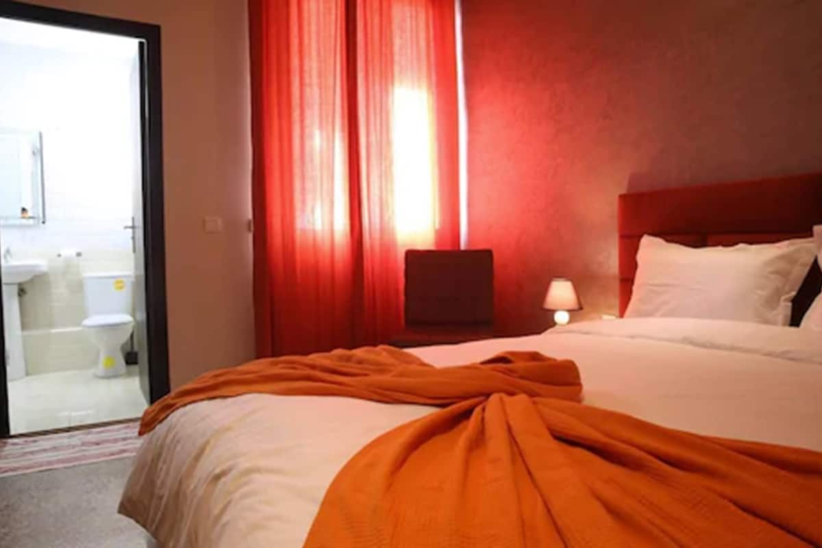 A hotel room with a bed, a nightstand, a lamp, and a view of the bathroom.