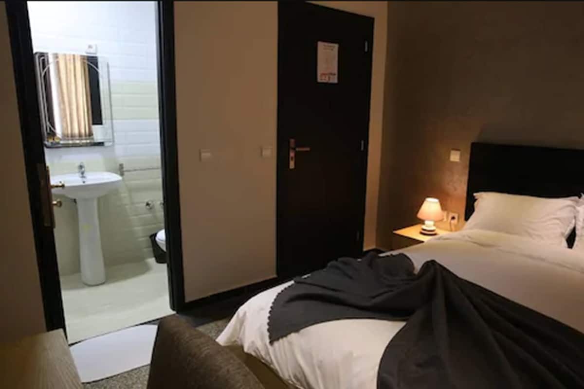 A hotel room with a bed, a bedside lamp, a nightstand, and a door leading to a bathroom.