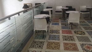 Een hotel lobby met een glazen balustrade, betegelde vloer en verschillende tafels en stoelen.