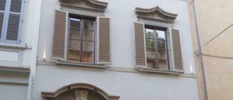 Un edificio de varios pisos con una entrada central, ventanas grandes con contraventanas y un arco de piedra a la derecha.