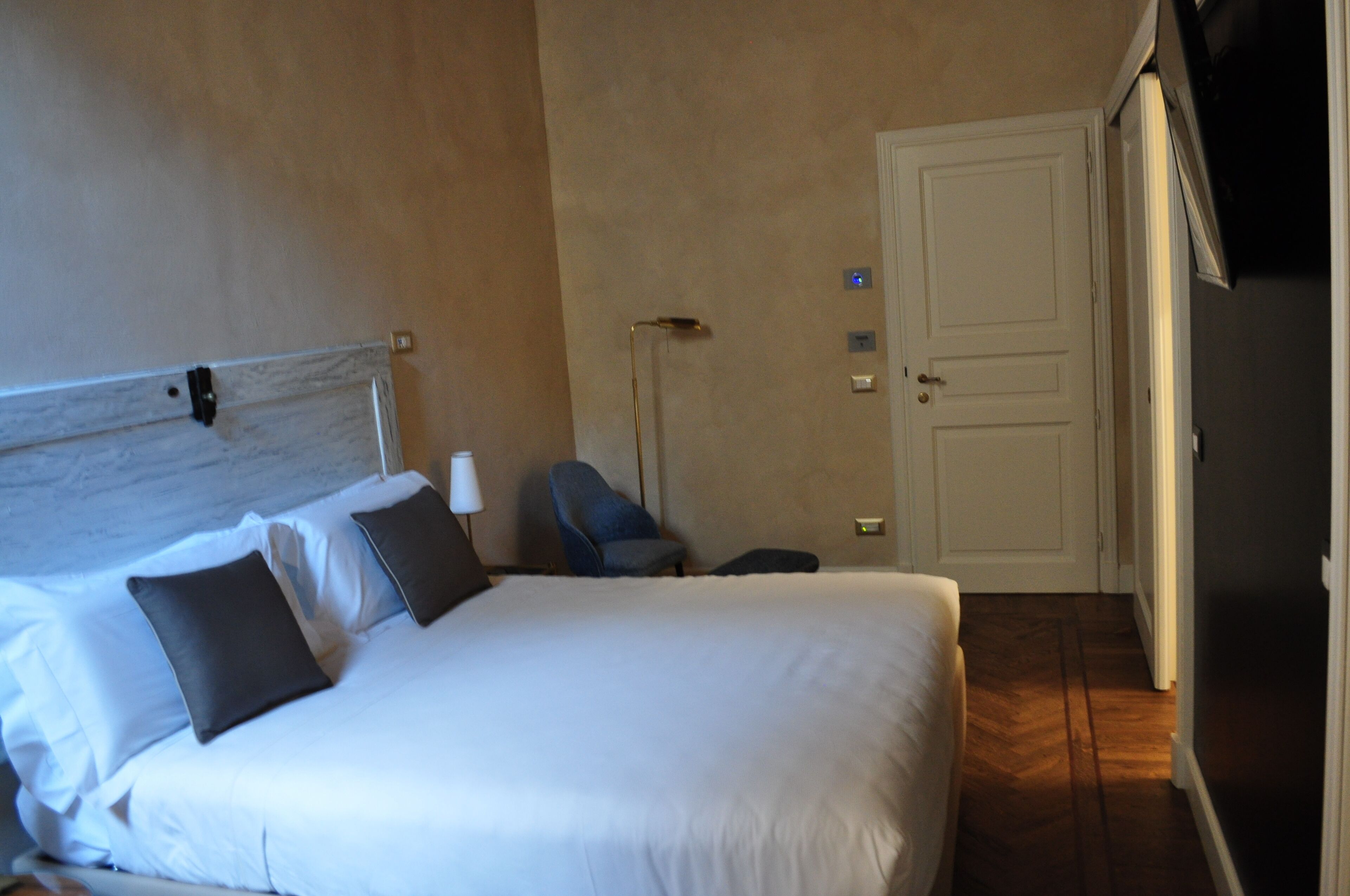 Ein Hotelzimmer mit Bett, Sessel, Lampe und Tür.