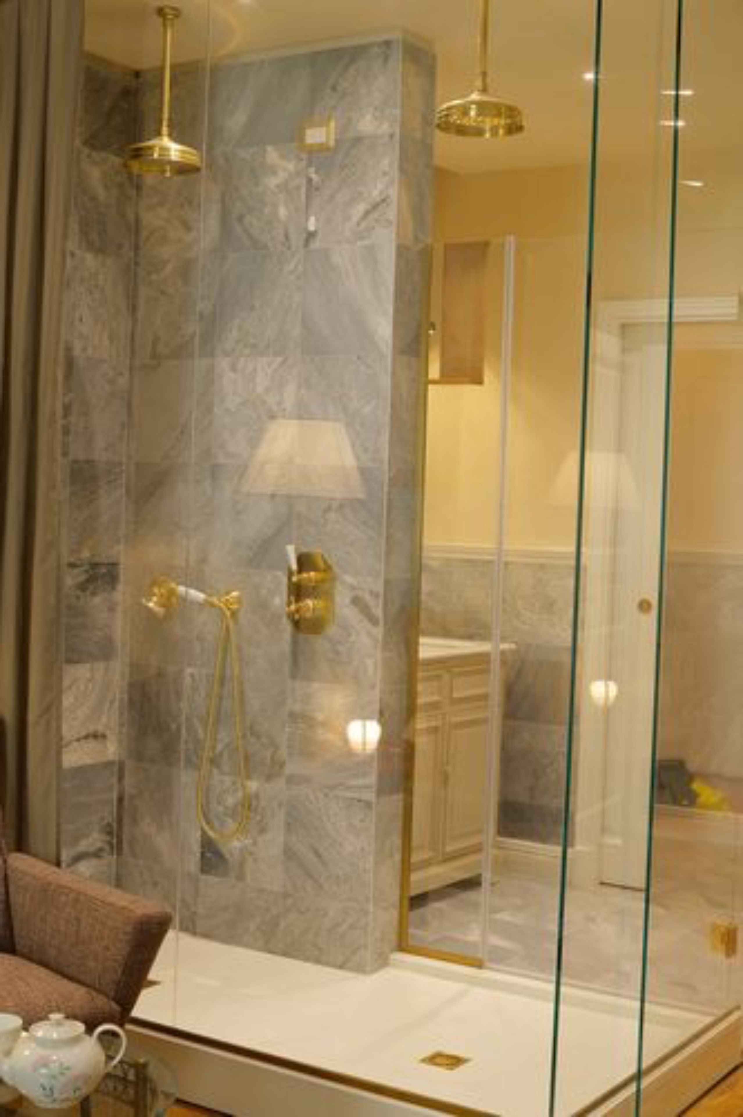 Un baño moderno con cabina de ducha de vidrio, paredes de mármol y grifería dorada.