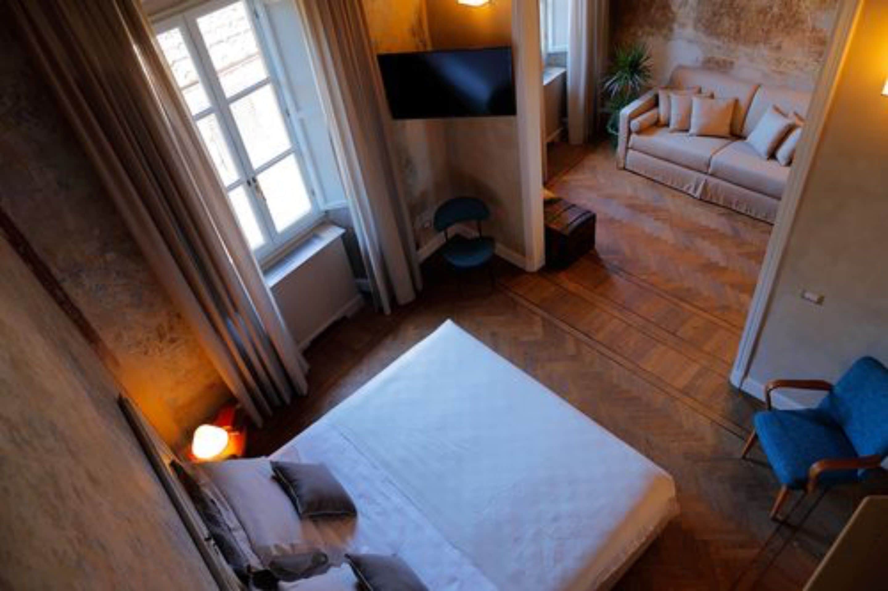 Une chambre à coucher avec un lit, un téléviseur fixé au mur, un canapé et un fauteuil.