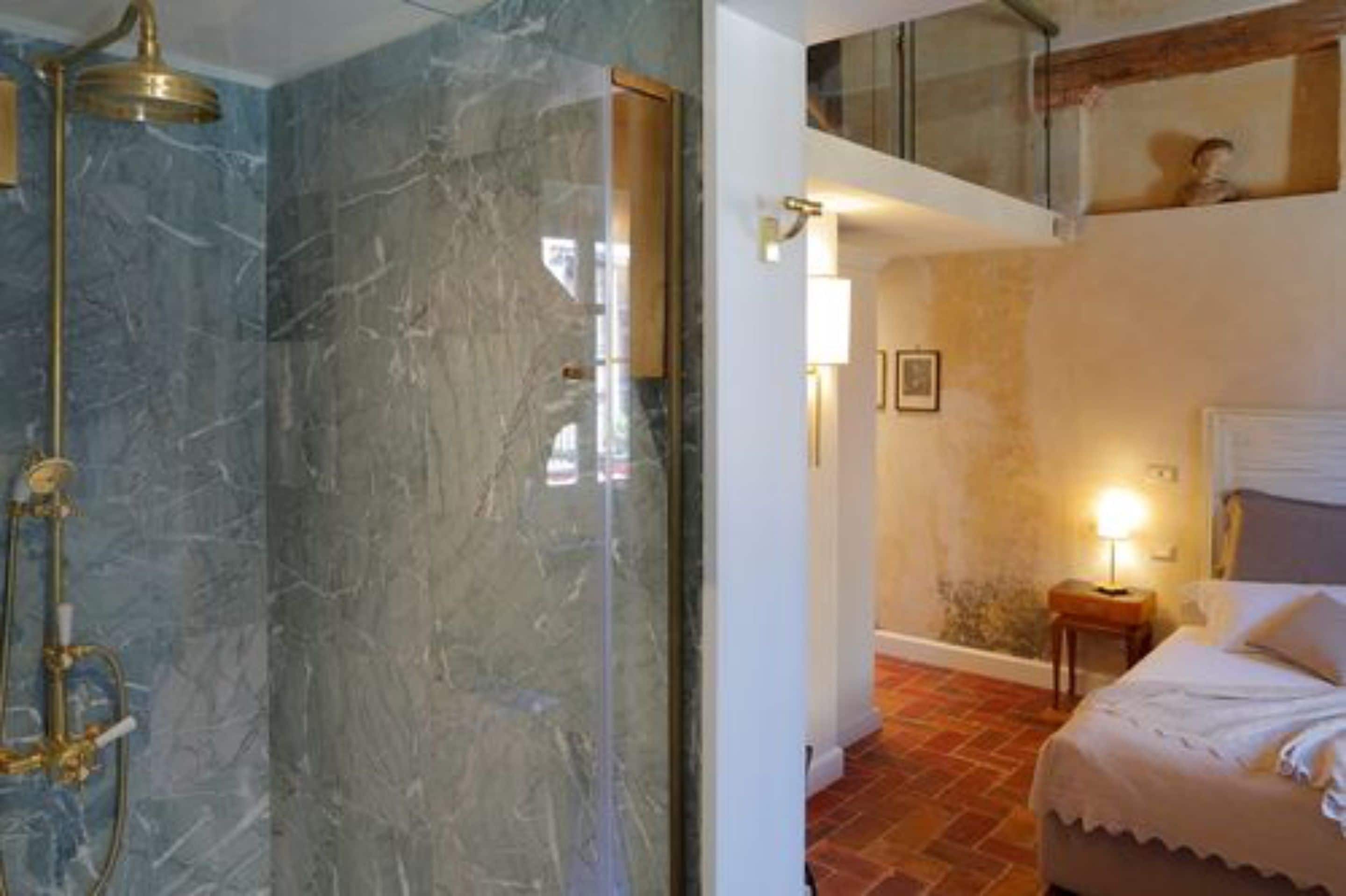 Une salle de bain avec une douche en marbre et une chambre à coucher avec un lit et une table de chevet.