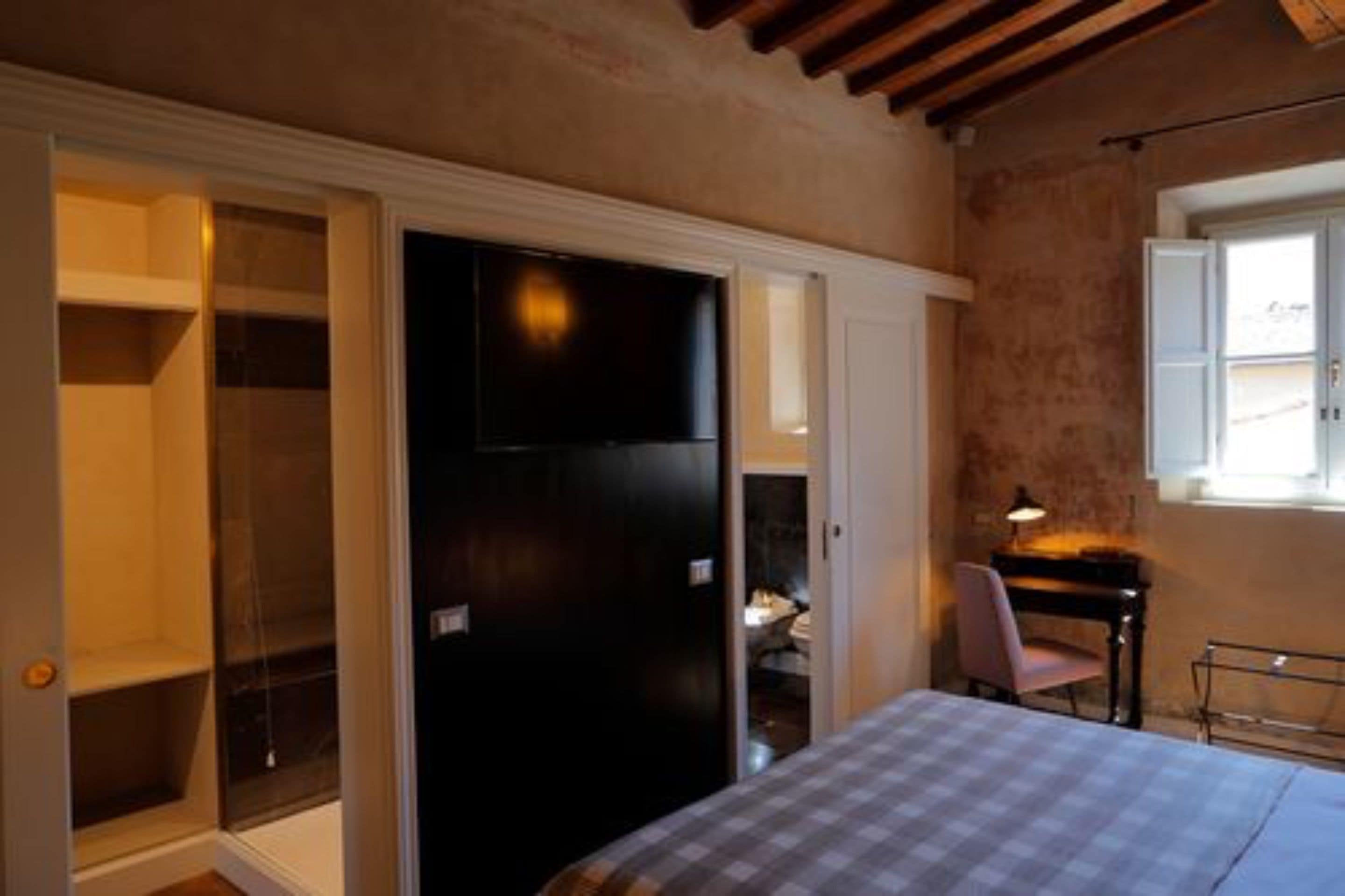 Una camera da letto con un letto, una scrivania e una sedia. Si trova un armadio con ante scorrevoli e una piccola finestra.