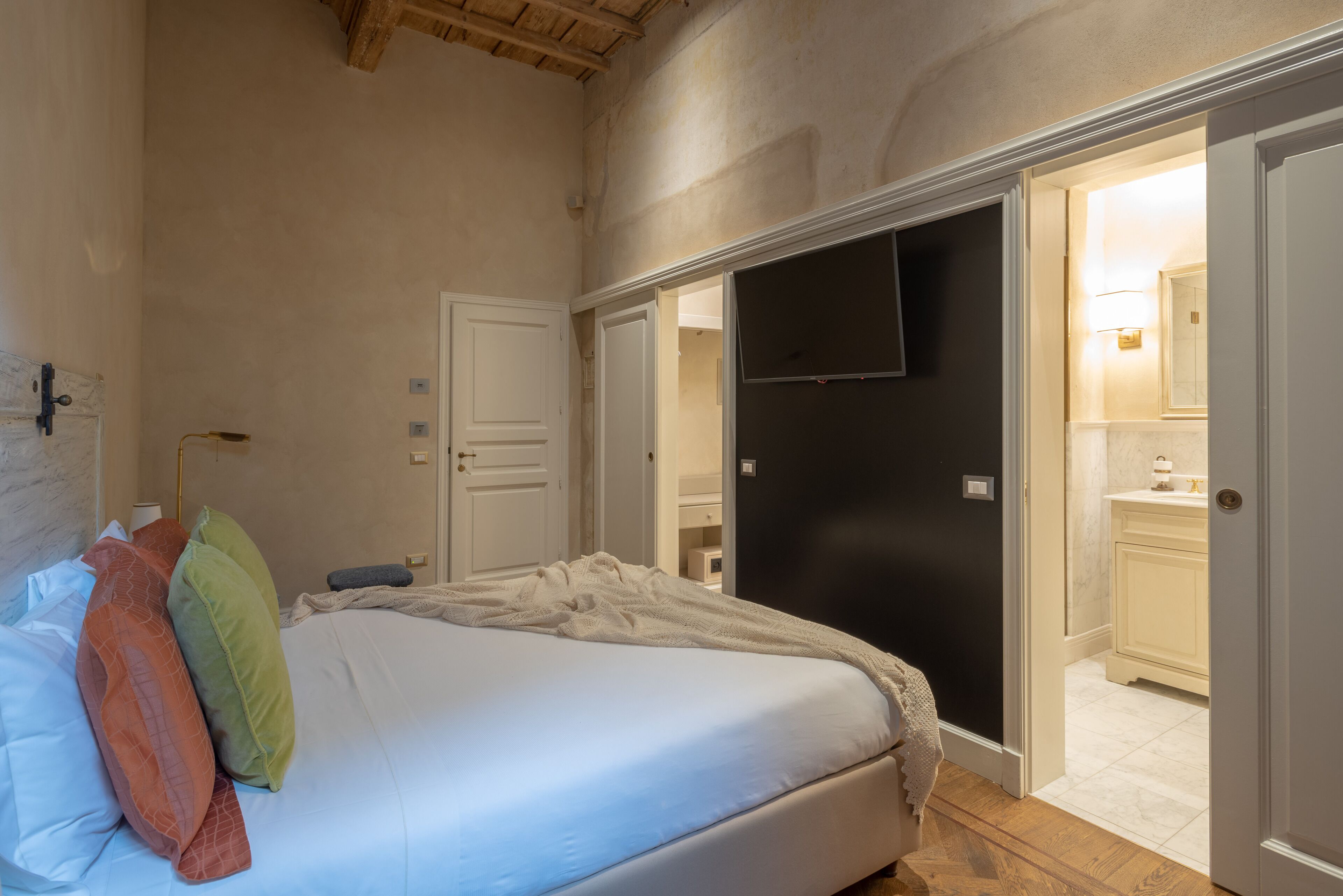 A bedroom with a bed, pillows, a flat-screen TV, and a door leading to a bathroom.