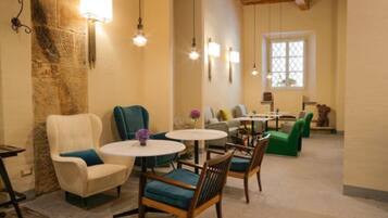 A cozy lounge area with round tables and chairs, stone walls, and hanging light fixtures.