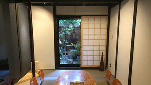 Une pièce de style japonais traditionnel, avec des tatamis servant de sièges, une table basse et une porte coulissante donnant sur un jardin.