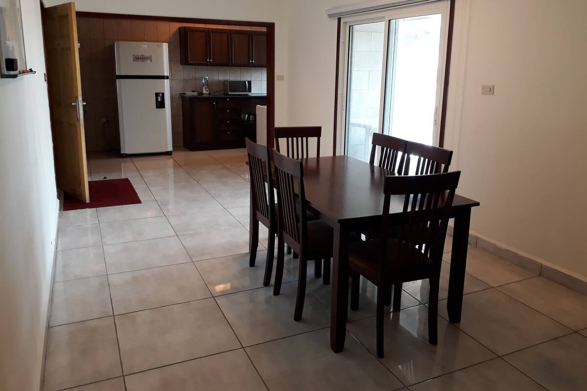 A dining area with a table and chairs, a kitchen with a refrigerator and microwave, and a sliding glass door to the outside.