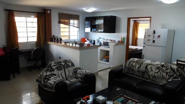 A living room with two sofas, a coffee table, a TV, and a kitchen area with a fridge and microwave.