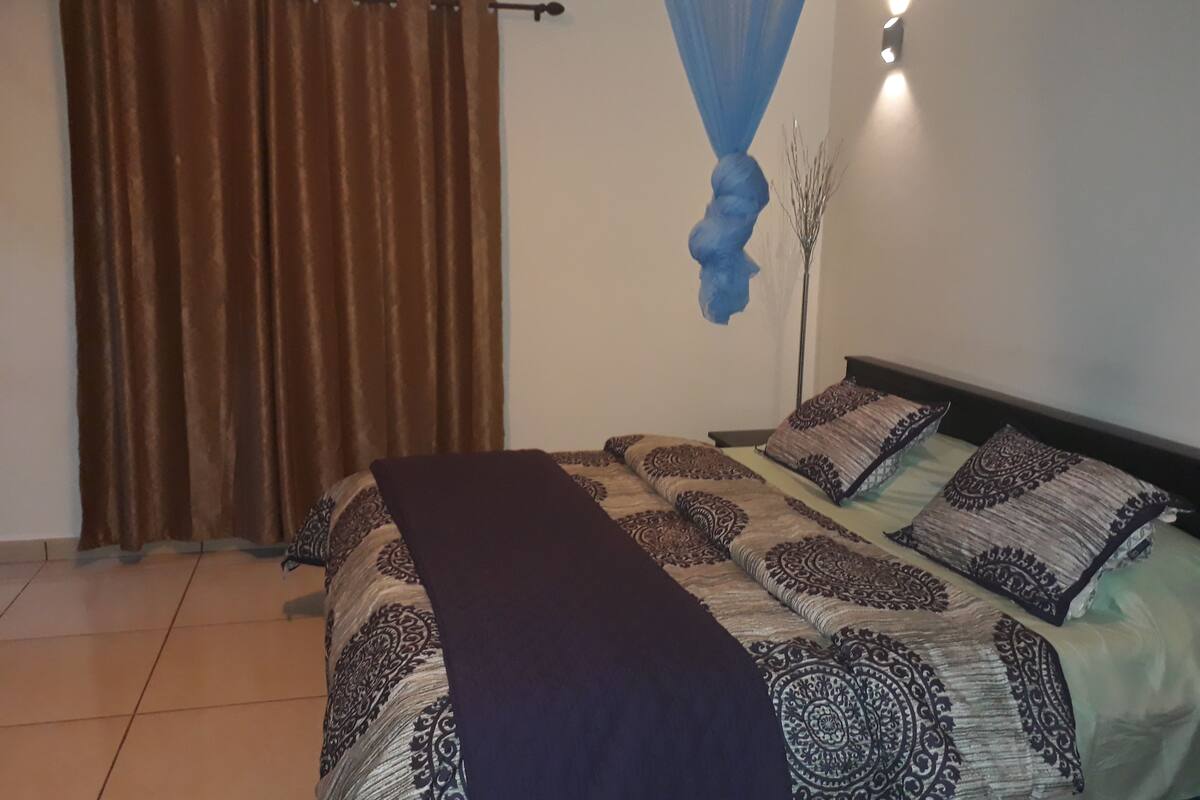 A bedroom with a bed, curtains, a hanging blue canopy, and a floor lamp.