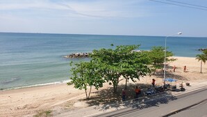 A beach with clear skies, calm sea, and a few people. There are trees and a streetlight visible. - Banchaitalay Room (Rayong)