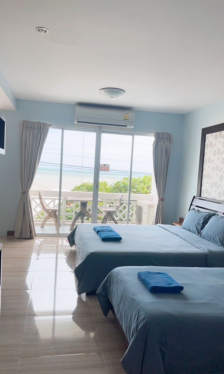 A hotel room with two beds, a balcony, and a view of the sea.