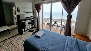 A hotel room with a bed, a desk, a chair, and a view of the sea through large windows. - Banchaitalay Room (Rayong)