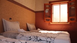 Habitación de hotel con dos camas, una ventana con contraventanas de madera y una pequeña mesa.