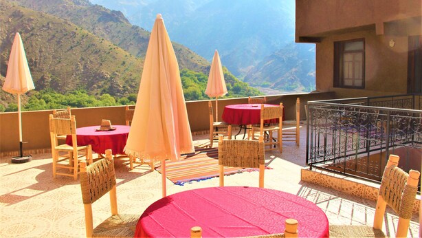 Una terraza con mesas y sillas, un mantel rojo y vistas a las montañas.
