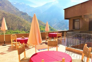 Una terraza con mesas y sillas, un mantel rojo y vistas a las montañas.