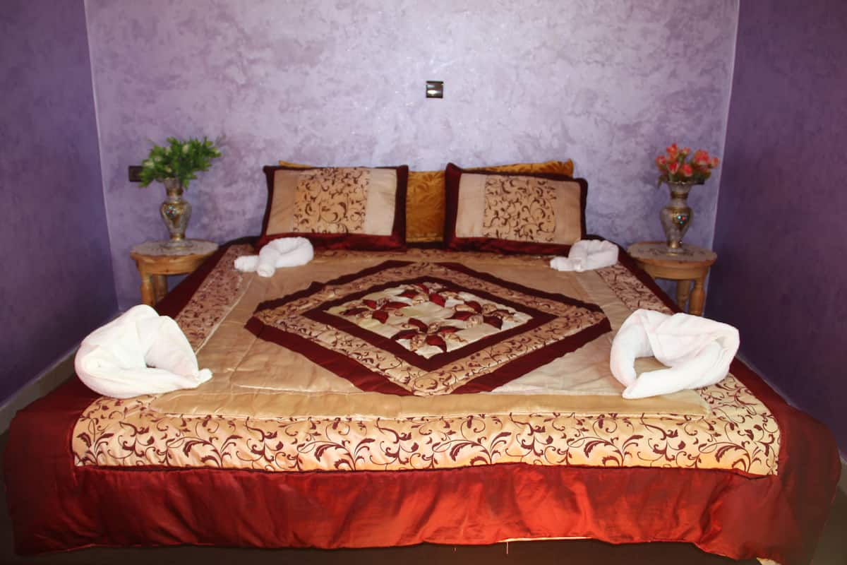 A neatly made bed with a patterned bedspread and pillows, two side tables with vases, and a small wall-mounted light.
