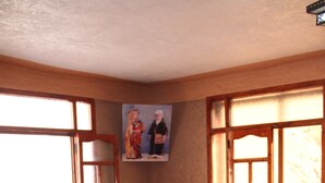 Una habitación con una mesa redonda, seis sillas de mimbre, un mantel rojo, cojines estampados y un cuadro en la pared.