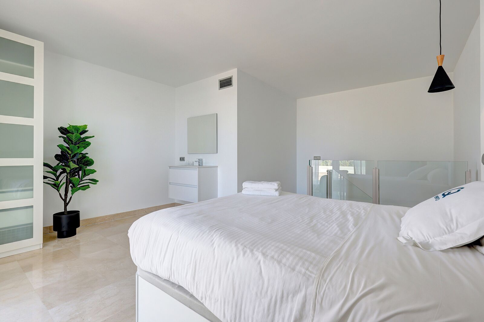 Un dormitorio moderno con una cama grande, una planta en maceta, una mesita de noche, un espejo y una ventana con cerramiento de vidrio.