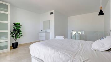 Un dormitorio moderno con una cama grande, una planta en maceta, una mesita de noche, un espejo y una ventana con cerramiento de vidrio.