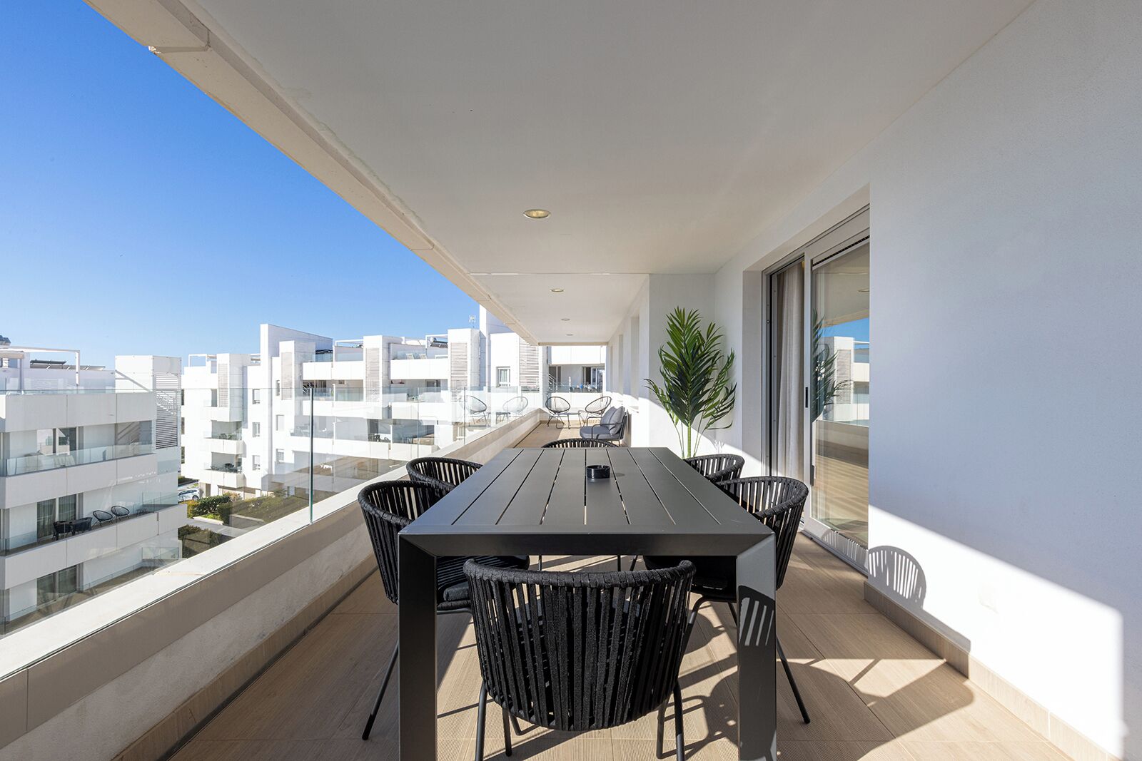 A balcony with a wooden table and chairs, overlooking a cityscape with modern buildings.