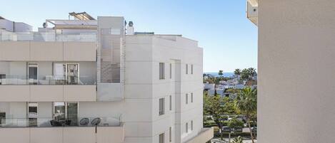 A modern multi-story building with balconies, large windows, and a clear view of the sea.