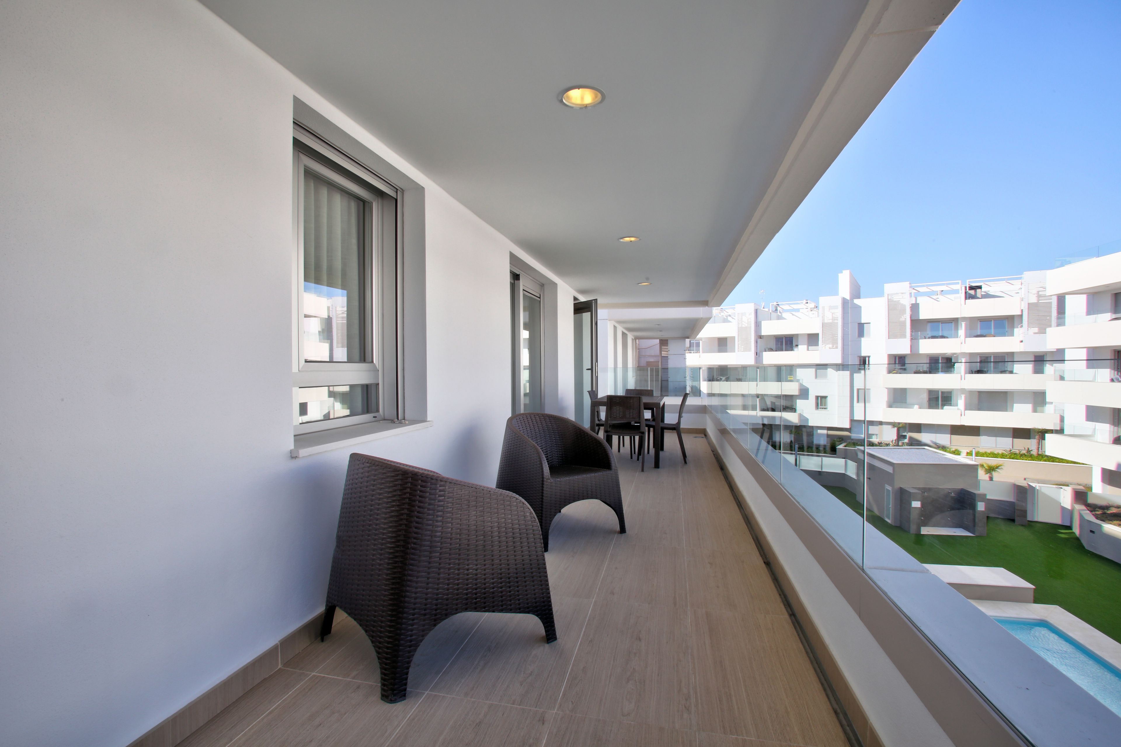 Un balcón con sillas de mimbre, una mesa de comedor y vistas a un moderno complejo de edificios.
