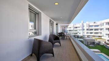 Un balcón con sillas de mimbre, una mesa de comedor y vistas a un moderno complejo de edificios.