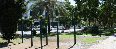 Un espacio exterior para ejercitarse con una estructura metálica, rodeado de árboles y una carretera con coches.