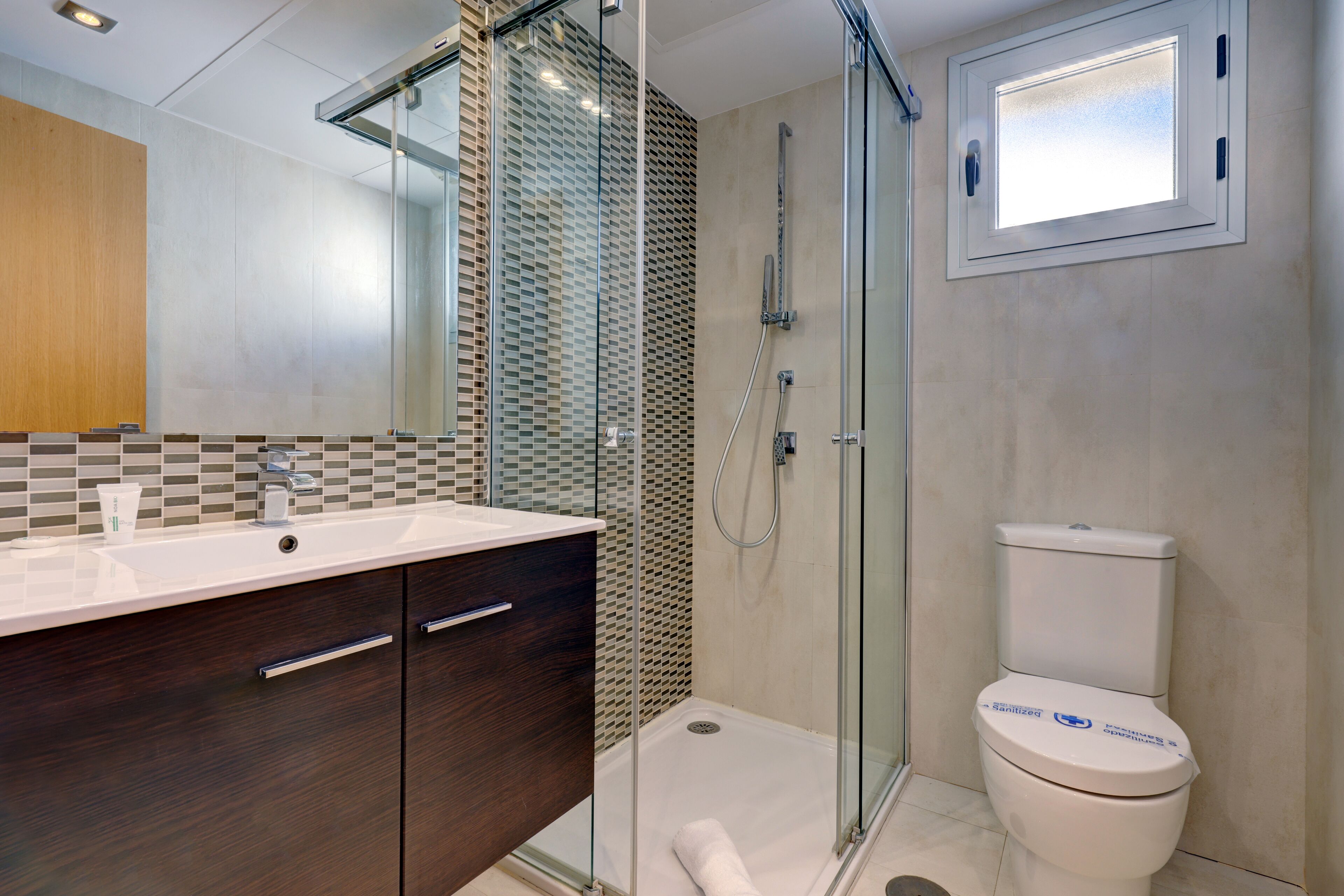 A modern bathroom with a glass-enclosed shower, a white toilet, and a vanity with a mirror.