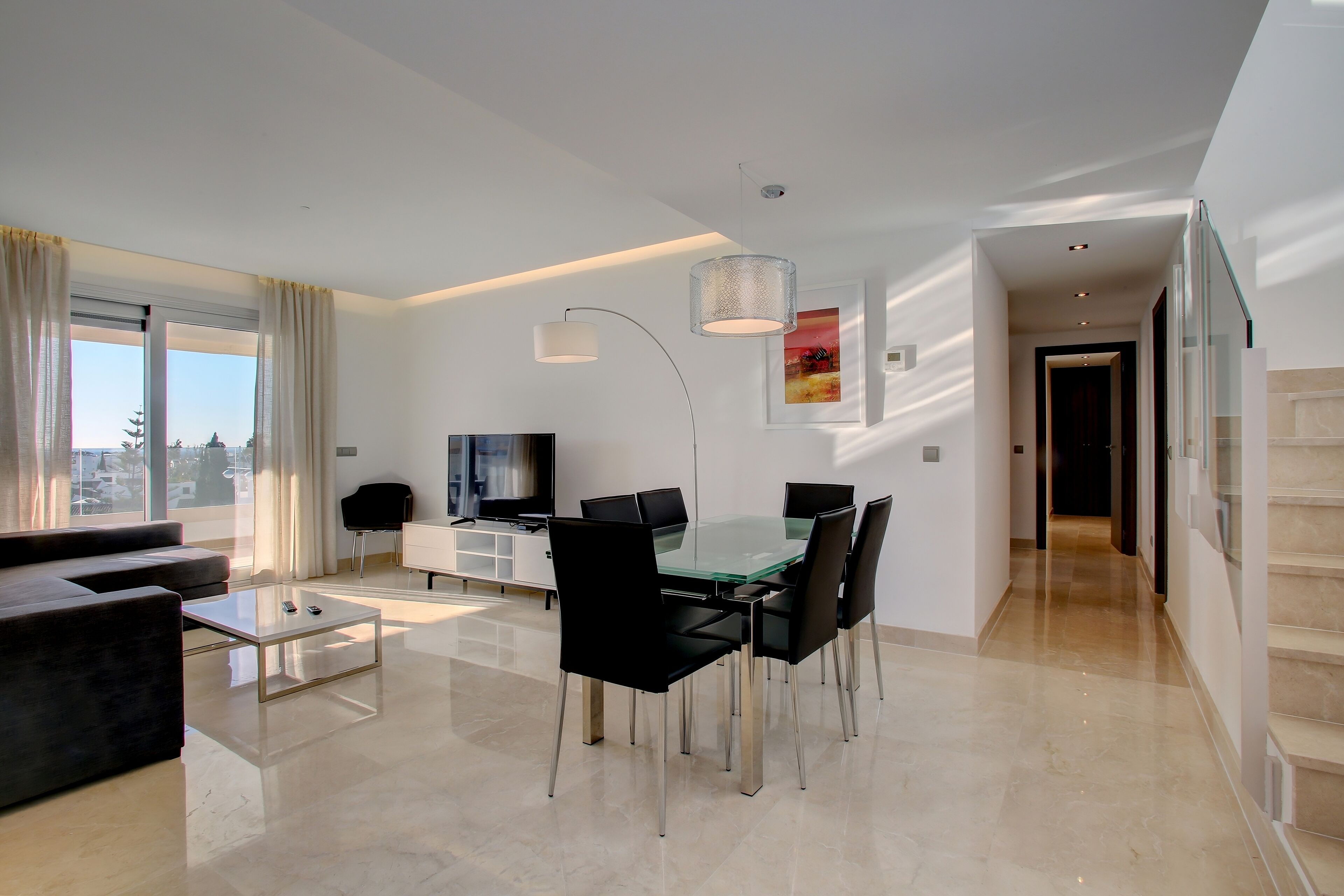 A modern living room with a glass dining table, black chairs, a sofa, and a TV.